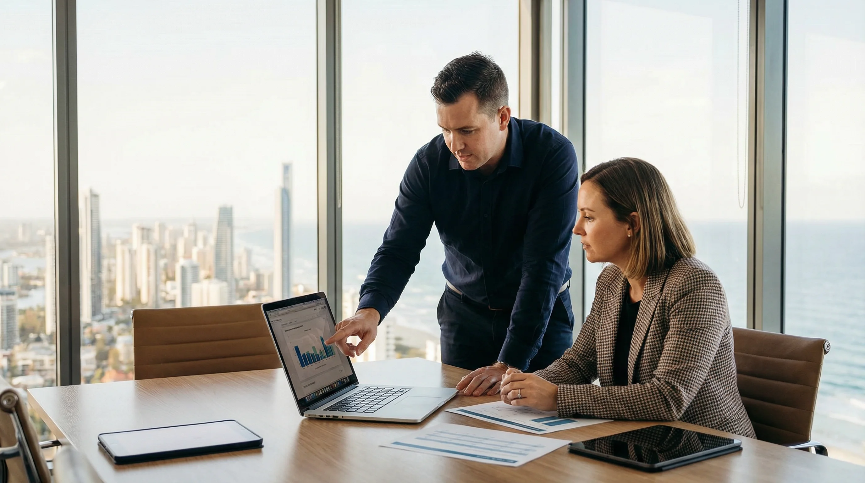 IT consultant reviewing technology strategy with a Gold Coast business owner in a modern office with coastal views